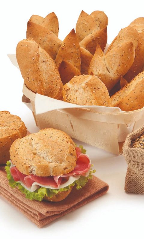 Panini multicereali in un cestino di legno, un panino farcito con prosciutto e lattuga e un sacco di juta con semi di...