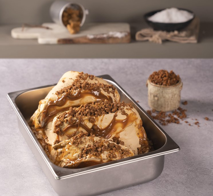 Gelato al caramello nella vaschetta, guarnito con pezzetti croccanti di toffee e vasetto di topping