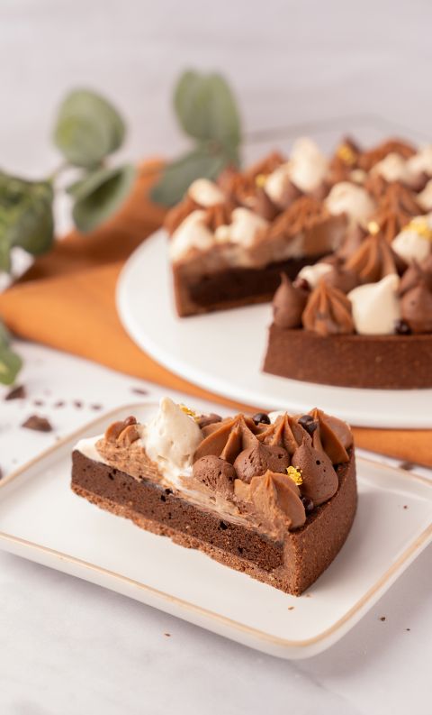 Fetta di crostata al cioccolato con panna decorata e rosette di cioccolato su piatto bianco, sfondo sfocato arancione