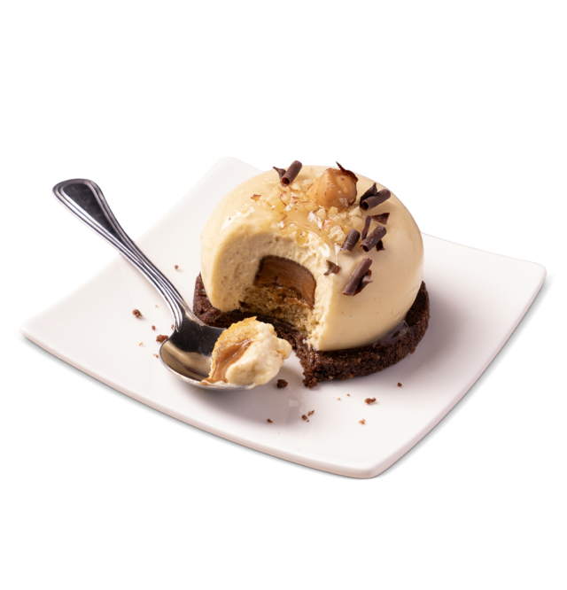 Mousse al caramello a cupola su base di biscotto al cioccolato, con nocciole e riccioli di cioccolato, con un morso