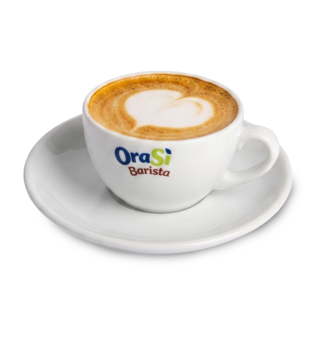Tazza bianca da cappuccino con latte art a forma di cuore, etichetta "OraSì Barista", su piattino coordinato su sfond...