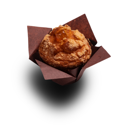 Muffin dorato con crumble di streusel e ripieno di frutta, in pirottino di carta marrone su sfondo bianco.