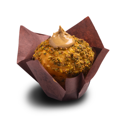 Muffin ricoperto di granella di pistacchio, con ciuffo di glassa al caramello, in pirottino tulipano marrone.