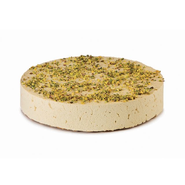 Disco rotondo di halva chiara con granella di pistacchio, texture densa e friabile, su sfondo bianco.
