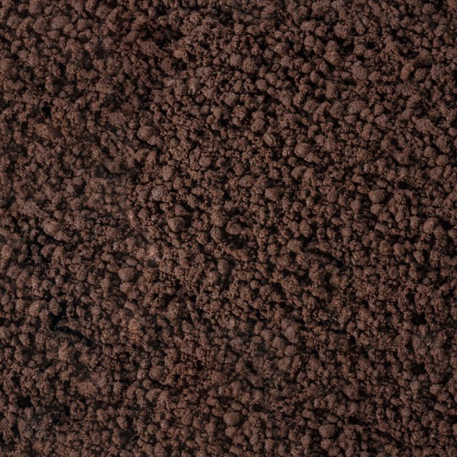 Primo piano di una superficie marrone scuro e granulosa, simile a terra grossolana o caffè macinato.