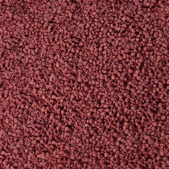 Texture ravvicinata di granuli o polvere grezza bruno-rossastra, simile a grani minerali o spezie agglomerate