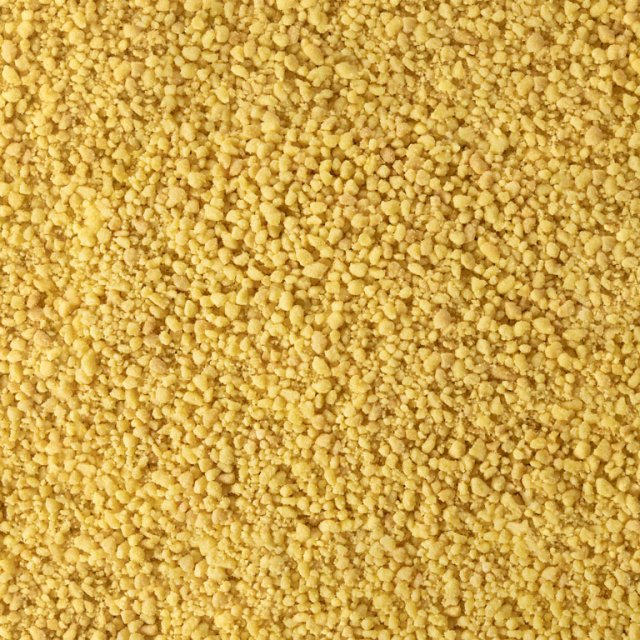 Primo piano di texture granulare gialla fine, simile a semola grossa o couscous secco.