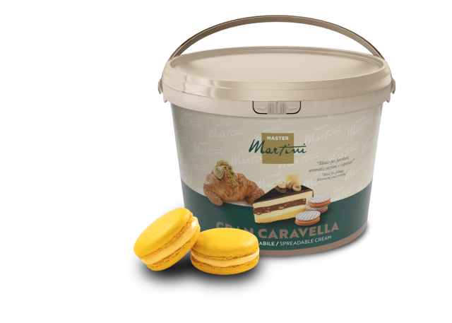 Secchiello beige di crema spalmabile Master Martini Gran Caravella accanto a due macaron gialli e un dolce farcito.