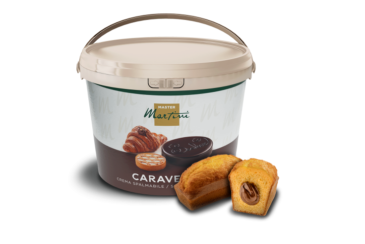 Secchiello grande di crema spalmabile Master Martini Caravella accanto a una mini torta ripiena di crema al cioccolato.