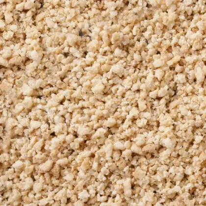 Primo piano di granuli beige chiari e sbriciolati, con texture grossolana simile a briciole.