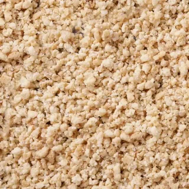 Primo piano di granuli beige chiari e sbriciolati, con texture grossolana simile a briciole.