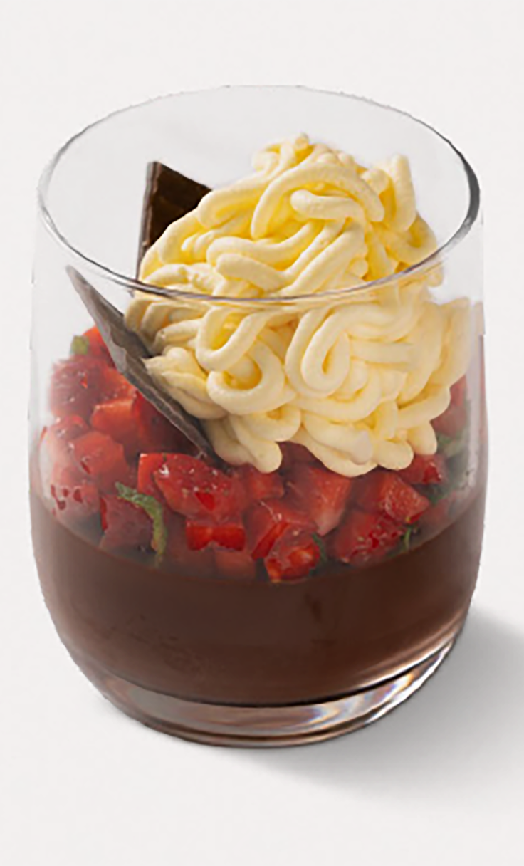 Dessert in bicchiere con mousse al cioccolato, fragole a cubetti e ciuffo di panna, scaglia di cioccolato