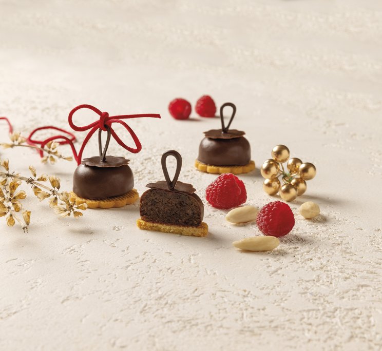 Dolcetti al cioccolato su base di biscotto, uno tagliato, con lamponi, mandorle e nastro rosso.
