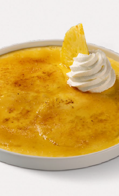 Crema catalana in pirofila bianca con zucchero caramellato, panna montata e spicchio d’ananas
