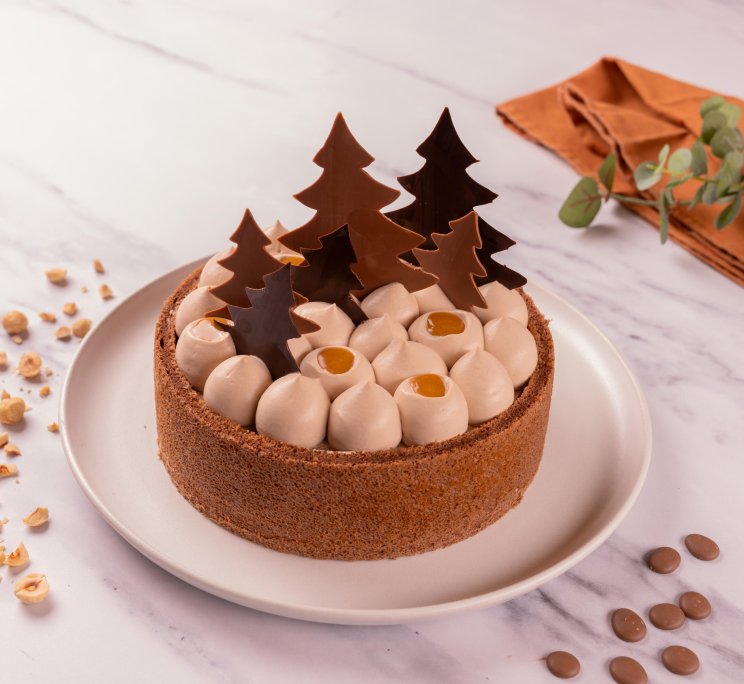 Crostata rotonda con ciuffi di crema, punti di caramello e decorazioni di cioccolato a forma di albero, circondata da...