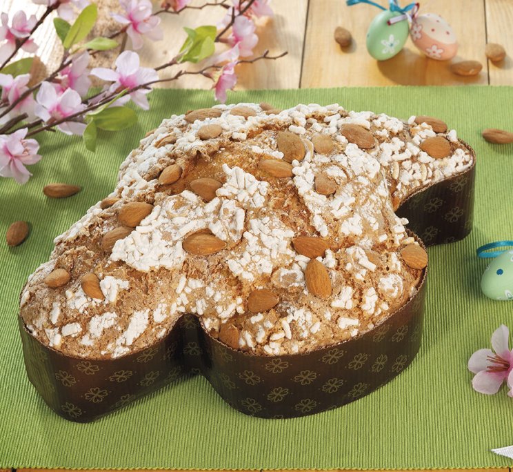 Colomba pasquale a forma di colomba con mandorle e granella di zucchero, su tappetino verde con fiori rosa.