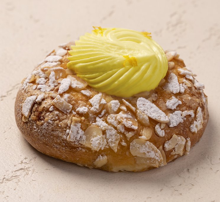Pasticcino con crema al limone gialla e vorticosa, spolverato di zucchero a velo e mandorle a scaglie tritate, su sfo...