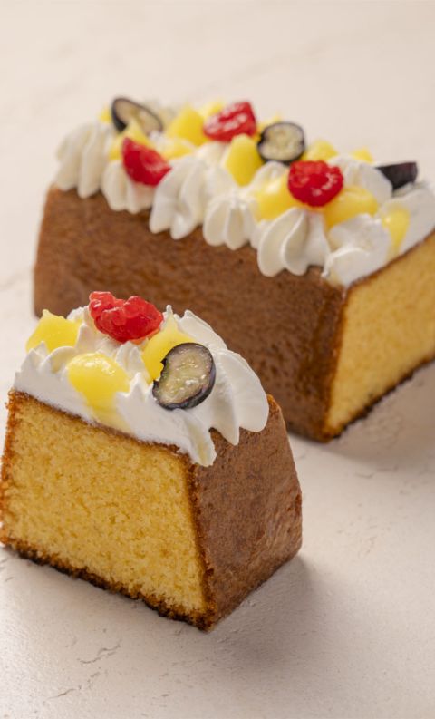 Torta intera e una fetta tagliata con panna, ananas candito, ciliegie e uva nera.