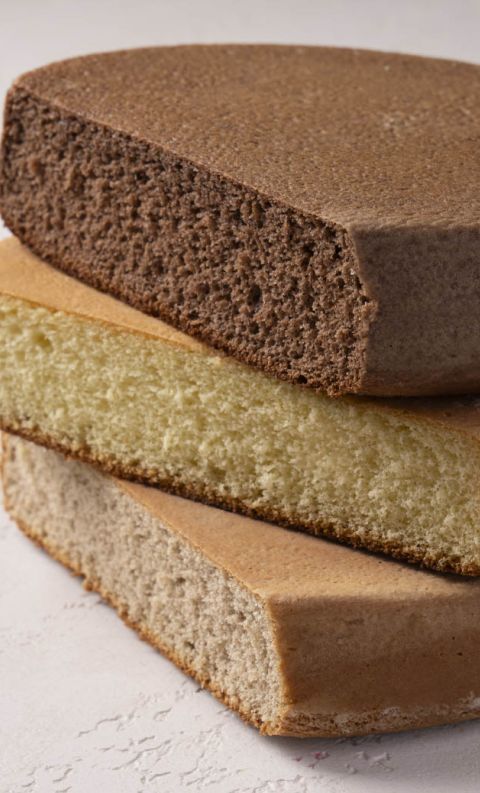Tre strati rotondi di pan di Spagna al cioccolato, pistacchio e vaniglia su superficie bianca.