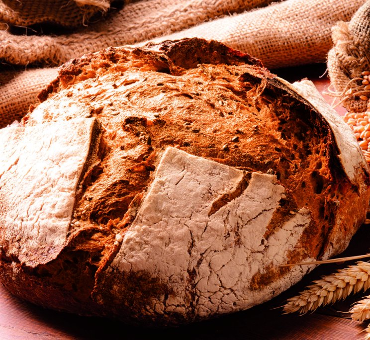 Pagnotta rustica croccante con crepe infarinate, su tavolo in legno con chicchi di grano e iuta.