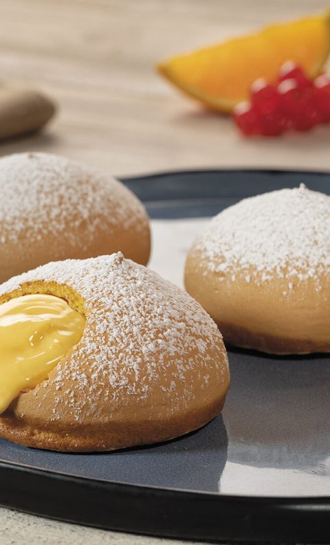 Tre paste zuccherate ripiene di crema pasticcera su piatto grigio scuro, con ribes arancioni e rossi intorno