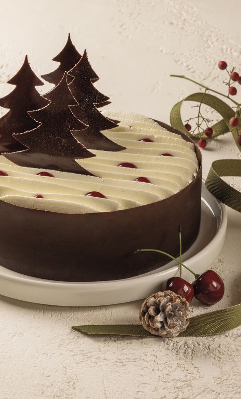 Torta di Natale rotonda al cioccolato con ciuffi di panna, ciliegie e decorazioni ad albero di cioccolato, con nastro