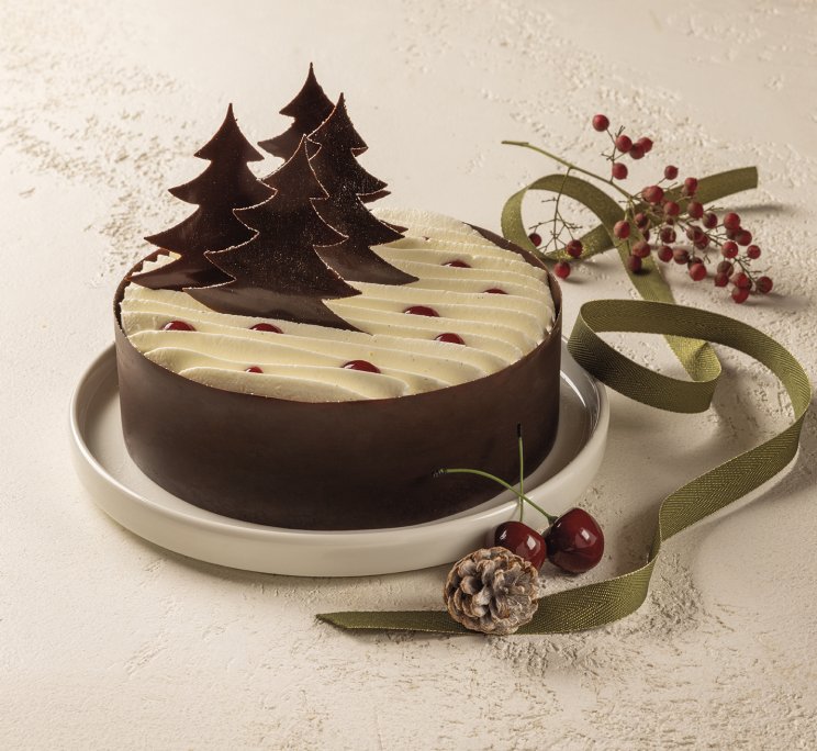 Torta di Natale rotonda al cioccolato con ciuffi di panna, ciliegie e decorazioni ad albero di cioccolato, con nastro