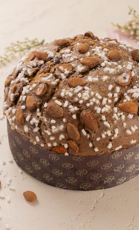 Panettone rotondo con mandorle intere e granella di zucchero, in involucro scuro decorato su sfondo chiaro con rametti