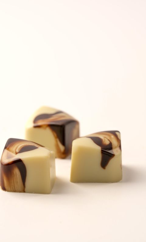 Tre praline di cioccolato bianco a forma di cubo con venature di cioccolato fondente su sfondo bianco.