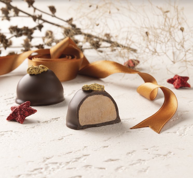 Due tartufi al cioccolato a cupola con foglia oro, uno tagliato, con nastro dorato e stelle rosse decorative.