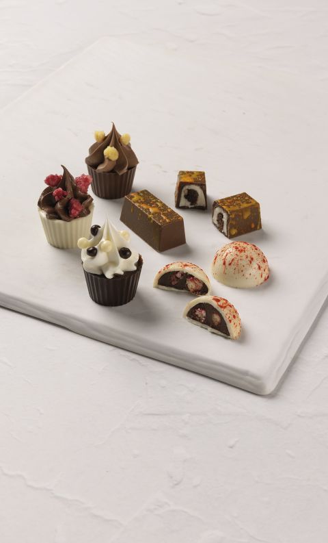 Assortimento di cioccolatini gourmet, con coppette alla crema e praline ripiene, su lastra di marmo bianco.