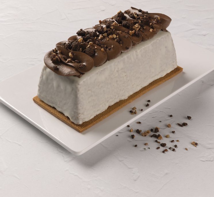 Semifreddo bianco rettangolare con riccioli di cioccolato e granella di nocciole, su piatto bianco.
