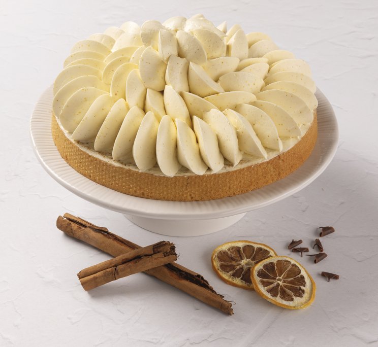 Crostata rotonda su alzata bianca, con petali di crema, bastoncini di cannella e fette di agrumi essiccati