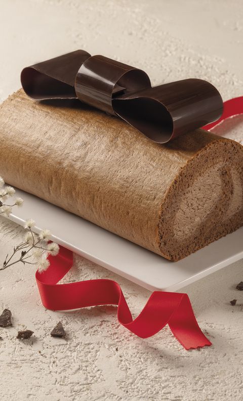 Torta arrotolata decorata con fiocco di cioccolato, nastro rosso, baccelli di vaniglia e fiori bianchi
