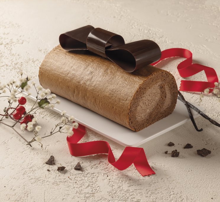 Torta arrotolata decorata con fiocco di cioccolato, nastro rosso, baccelli di vaniglia e fiori bianchi