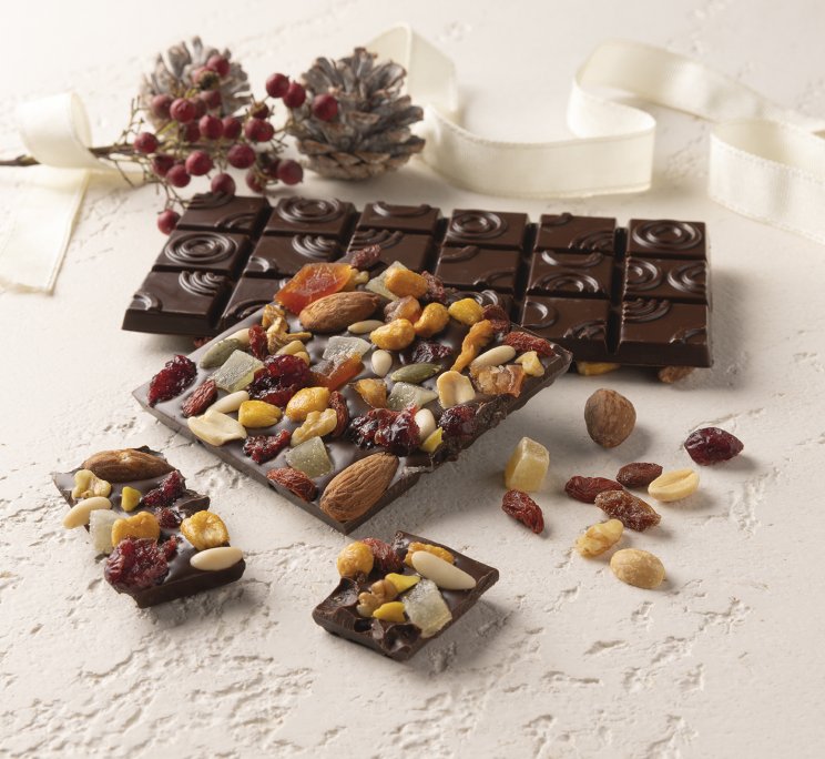 Barrette di cioccolato fondente con frutta secca e disidratata, con una barretta liscia e nastro natalizio sullo sfondo.