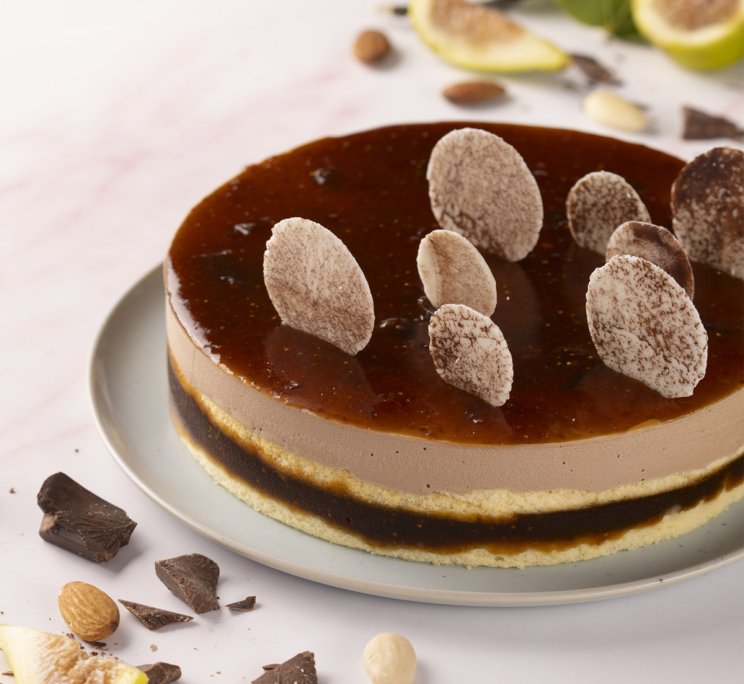 Torta tonda con mousse al cioccolato, glassa lucida al caramello e riccioli di cioccolato, su piatto con mandorle
