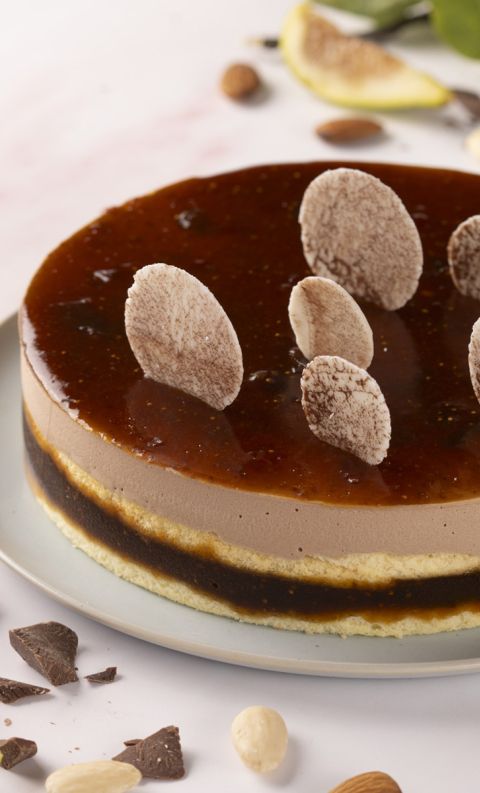 Torta tonda con mousse al cioccolato, glassa lucida al caramello e riccioli di cioccolato, su piatto con mandorle