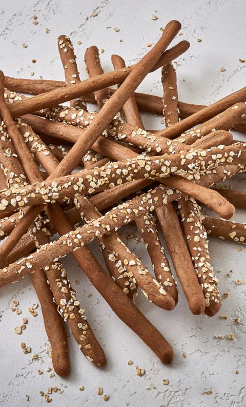 Mucchio disordinato di grissini integrali con avena su una superficie bianca testurizzata.
