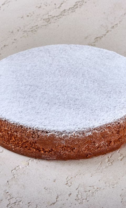 Torta rotonda dorata cosparsa di zucchero a velo su superficie grigia texturizzata.