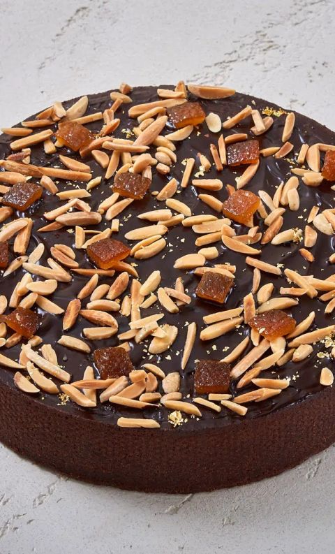 Crostata rotonda al cioccolato con mandorle tostate a lamelle e scorza d'arancia candita su superficie grigia testuri...